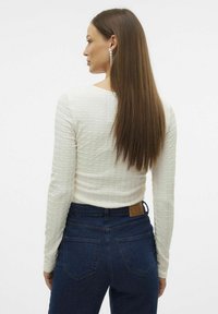 Langermet hvit teksturert topp med rund hals, kombinert med høyt liv mørkeblå jeans som har baklommer og lærlogo.
