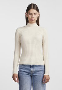 Krämfärgad ribbad polo-tröja med långa ärmar, figurnära silhuett och lätt textur, kombinerad med blå jeans.