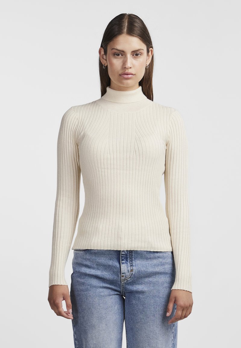 Krämfärgad ribbad polo-tröja med långa ärmar, figurnära silhuett och lätt textur, kombinerad med blå jeans.