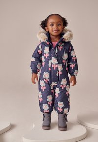 Combinezon de zăpadă bleumarin cu modele florale roz și verzi, glugă din blană sintetică, manșete elastice și cizme de iarnă gri. Material moale și călduros.