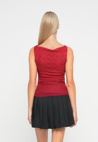 Crvena majica bez rukava s uzorkom točkica, nabranim dizajnom i izrezom u obliku slova V, u kombinaciji s crnom suknjom s plisiranjem.