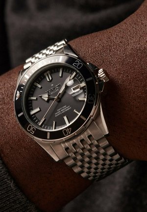 Silver stainless steel watch with a black dial, luminous markers, date window, and a textured metal bracelet. Water-resistant up to 100m.