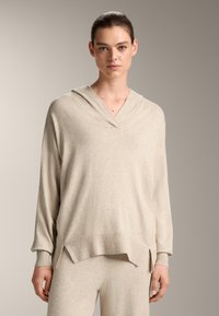 Beige hoodie met lange mouwen, een V-hals en geribbeld zoom. Zachte textuur en ontspannen pasvorm met zijsplits voor een gemakkelijke beweging.