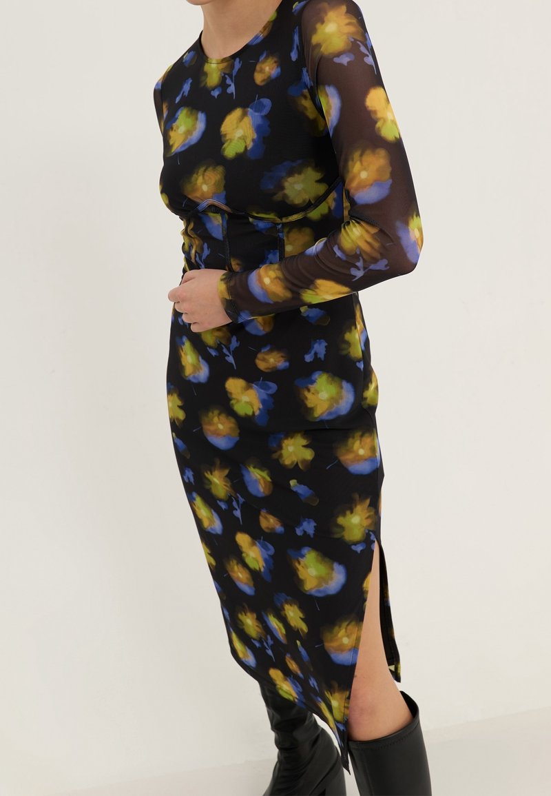 Langärmliges Kleid aus schwarzem Stoff mit blauen, gelben und grünen Blumenmustern; verfügt über seitliche Schlitze und eine taillierte Silhouette.