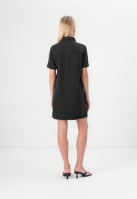 Zwarte denim jurk met korte mouwen, kraag en opgerolde manchetten, met een rechte snit en gestikte details bij de zoom.