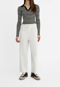 Haut à manches longues rayé noir et blanc associé à un pantalon blanc taille haute et des baskets noires avec des accents texturés et des lacets blancs.