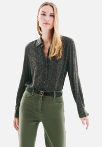 Chemise à manches longues à motifs verts, portée avec un pantalon vert taille haute et une ceinture noire avec une boucle rectangulaire en or.