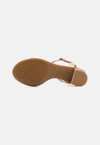 Brown rubber sole with textured grip, featuring a tan strap and metallic accents. Open design with a slender heel and a smooth finish.