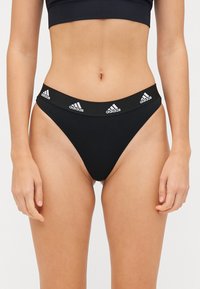 Melns augstas jostas bikīni apakšējā daļa ar elastīgu audumu, kuram ir baltas Adidas logo uz jostas un elegants, minimālistisks dizains.