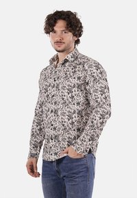 Camicia a maniche lunghe con bottoni, caratterizzata da un motivo floreale in bianco e nero su tessuto leggero. Collo classico e design aderente, indossata con jeans.