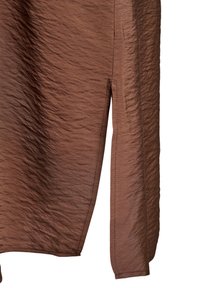 Gros plan d'une jupe en tissu marron texturé avec une fente latérale et des coutures visibles le long des bords.