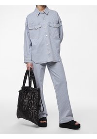 Randig denimskjorta med framfickor, i kombination med matchande byxor. Svart vadderad tote-väska och plattformssandaler.