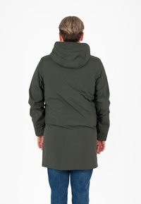 Giacca a vento verde oliva con cappuccio, dalla lunghezza lunga e polsini elasticizzati, caratterizzata da una texture liscia e opaca. Vista da dietro, indossata su pantaloni in denim blu.