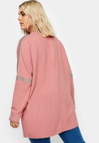 Pitkähihainen vaaleanpunainen collegepaita, jossa on rento istuvuus ja hopeiset niittikoristeet harteilla ja sivuilla. Pehmeä pinta, jossa on sileä viimeistely.