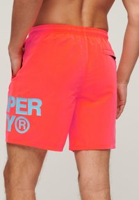 Felle roze zwembroek met een elastische tailleband, zijzakken en een groot blauw logo op het linkerbeen. Korte lengte en lichtgewicht materiaal.