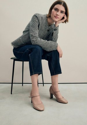 Beige patenterede læder hæle med en rem tværs over foran, parret med en struktureret grå jakke og mørke denim cropped jeans.