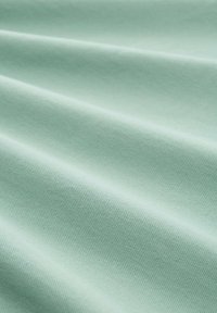 Tejido texturizado en verde claro con pliegues diagonales que crean sombras y reflejos suaves en la superficie.