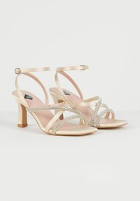 Sandali alti in satin beige con cinturini incrociati e dettagli in strass, dotati di una fascia alla caviglia e design con tacco a blocco.