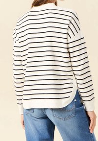 Striped sweater in cream with navy stripes, featuring a relaxed fit, ribbed cuffs, and a rounded hemline. Worn with blue denim jeans.