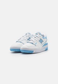 Paire de baskets New Balance 550 blanches et bleu clair avec lacets, logo de la marque sur les côtés et semelles texturées sur fond blanc.