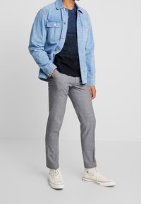 Veste en denim bleu clair, pull texturé bleu marine, pantalon à carreaux gris et baskets crème. Les caractéristiques clés comprennent des coutures détaillées et des motifs subtils.
