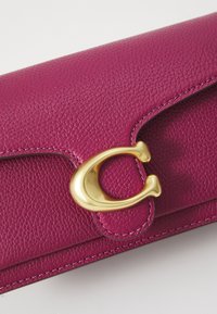 Magenta leather clutch with a textured finish, featuring a gold circular clasp and contrasting stitching along the edges.