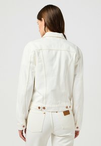 Vit denimjacka med krage, långa ärmar och knappdetaljer; har en texturerad tyg, synlig sömnad och ett märke på baksidan.
