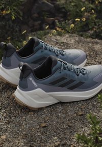 Graue Sportschuhe mit strukturiertem Obermaterial, schwarzen Akzenten und weißen Sohlen. Verfügt über eine hintere Schlaufe und ein atmungsaktives Design für Komfort.