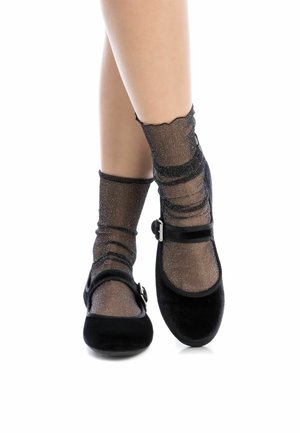 Zapatos Mary Jane de terciopelo negro con punta redondeada, correa con hebilla y calcetas negras brillantes con un diseño texturizado y acanalado.