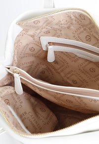 Interno della borsa bianca con una fodera beige caratterizzata da un motivo con il logo ripetuto "CAFE NOIR". Include una tasca con zip e due tasche a scomparsa.