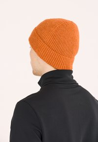 Orange ribbet strikhætte med en løstsiddende pasform, der har en glat overflade, står højt ved kronen, båret med en sort turtle neck.