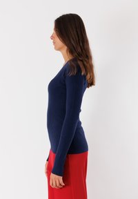 Maglione in maglia a coste blu navy con un design aderente, maniche lunghe e scollatura a V profonda, abbinato a pantaloni rossi a vita alta.