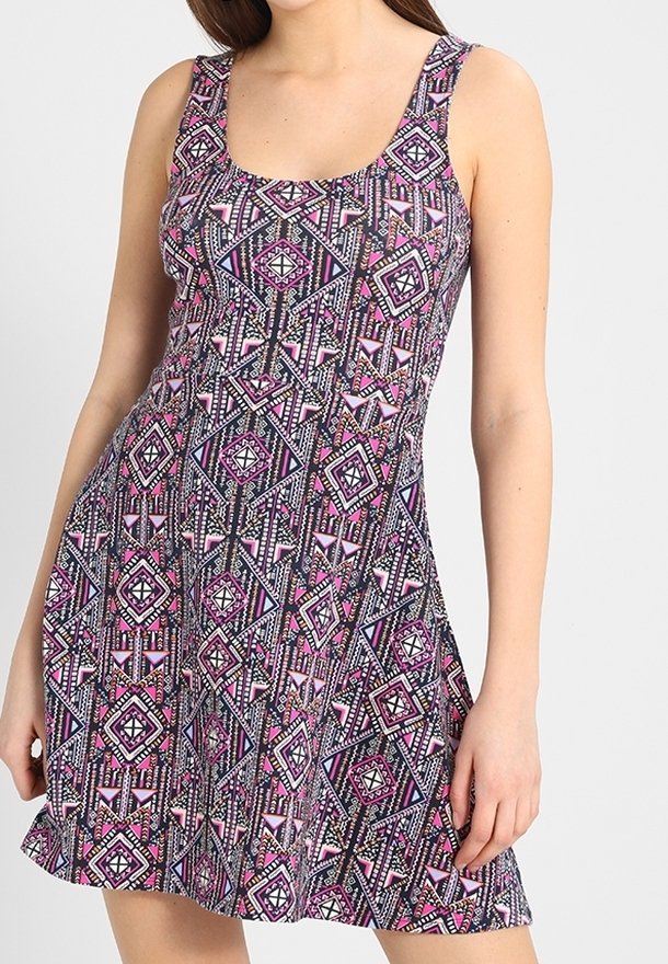 Vestido sin mangas en una tela elástica que presenta un patrón geométrico en tonos negro, rosa y púrpura. Diseño de escote redondo y falda acampanada.