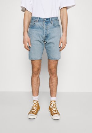 Persoon draagt lichtblauwe denim shorts, witte crew-sokken, mosterdgele hoge sneakers en een wit shirt met korte mouwen.