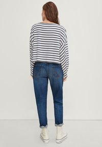 Top a maniche lunghe a righe, tagliato, in bianco e blu navy, abbinato a jeans blu con orli arrotolati e due tasche posteriori. Sneakers alte bianche.