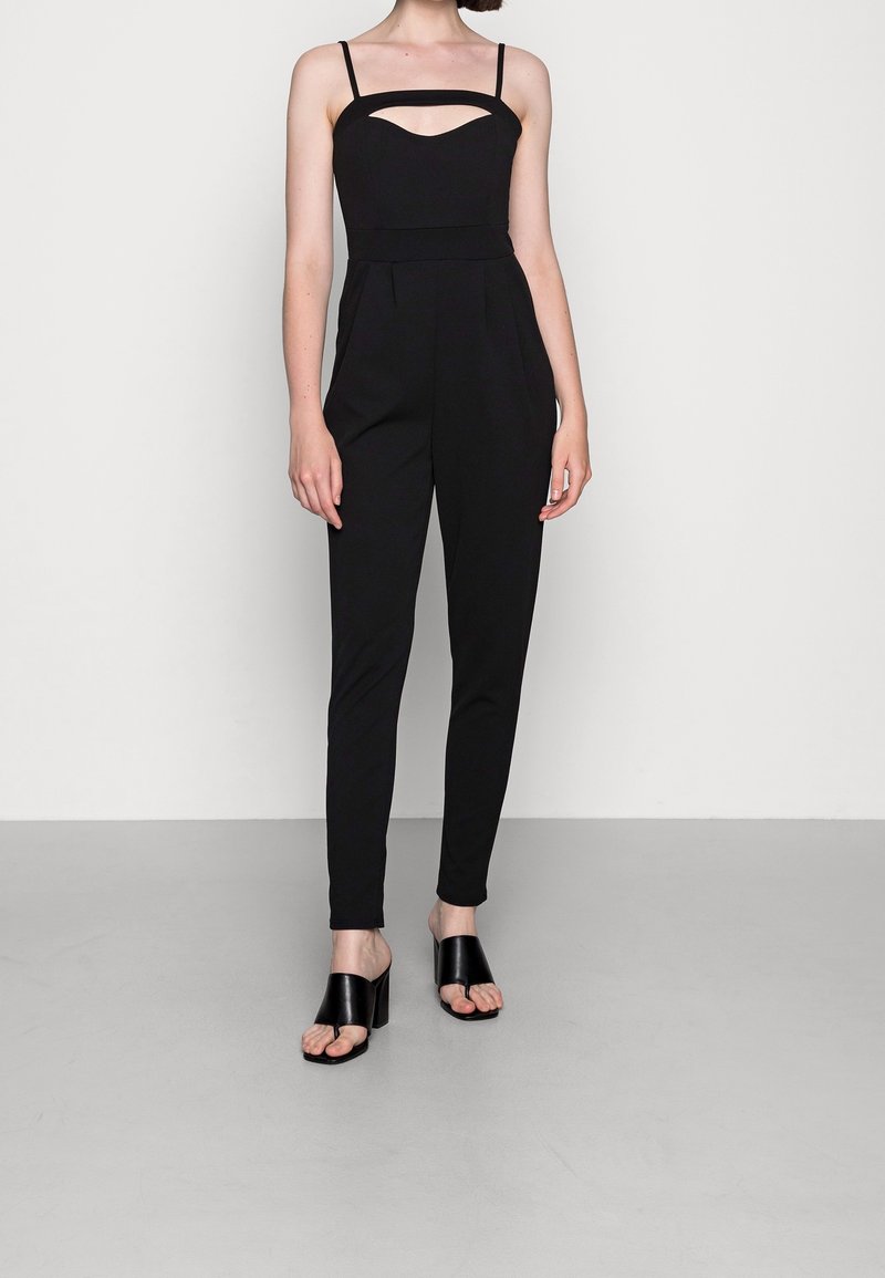 Svart jumpsuit med urklippt halsringning, små axelband, smalnande ben och minimalistisk design. I kombination med svarta sandaler med blockklack.