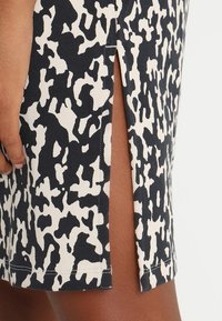 Černobílá sukně s abstraktním vzorem a bočním rozparkem, který odhaluje kůži, vedle odpočívající ruky s tmavou pleťovou barvou.