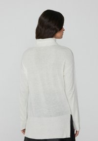 Cremfarbener Rollkragenpullover aus strukturiertem Stoff, mit langen Ärmeln und geripptem Saum, ausgestattet mit seitlichen Schlitzen für eine lockere Passform.