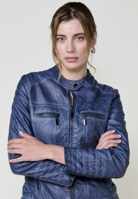 Giacca da moto in pelle blu navy con design strutturato, colletto alto, zip frontale e due tasche sul petto. Presenta cuciture trapuntate sulle maniche.