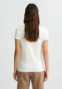 Korte mouwen, crèmekleurig T-shirt met een ronde halslijn. Gladde textuur, slim fit ontwerp, gecombineerd met beige, loszittende broeken.