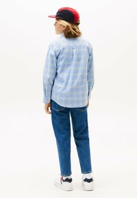 Camicia a quadri blu chiaro con maniche lunghe, abbinata a jeans blu e sneaker bianchi. Un cappellino rosso e blu completa il look.