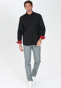 Chemise noire à boutons avec des poignets rouges, associée à un pantalon gris clair et des baskets blanches ; design simple, tissu lisse, coupe ajustée.