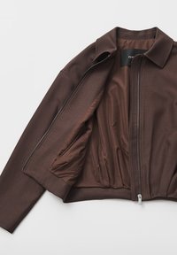 Giacca marrone con cerniera, esterno strutturato, morbida fodera interna e colletto. Presenta una texture raccolta in vita e una cerniera argentata.