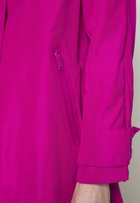 Fuchsia waterdichte jas met een ritssluiting op de mouw, een gladde textuur en een omgeslagen manchetdetail.