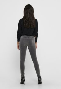 Šedé džíny skinny s upnutým střihem, vybavené zadními kapsami a jemným vyblednutím. Nosí se s černou košilí s dlouhým rukávem a vysokými podpatky.