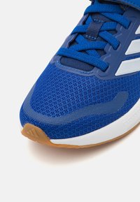 Chaussure de sport bleue avec une tige en textile en mesh, semelle en caoutchouc et accents blancs. Équipée de lacets plats et d'une texture antidérapante sur la semelle.