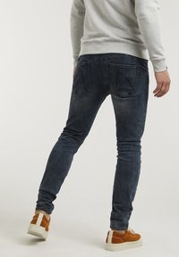 Smal passform mörkblå jeans i denim, med fem fickor, subtil blekning och detaljer vid ryggen. I kombination med bruna sneakers.