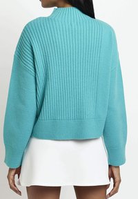 Tyrkysový pletený svetr s ribbovanou strukturou, vysokým límcem, oversized střihem a zkráceným lemem. Měkký materiál, široké rukávy a žádné viditelné zapínání.