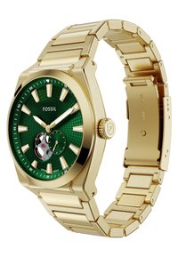 Guldtonet Fossil-ur med en grøn mønstret urskive, lysende timemarkører og et armbånd i rustfrit stål med lås.