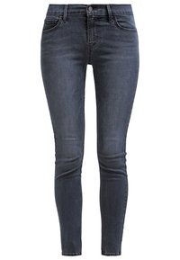 Jean en denim bleu foncé à coupe slim avec bouton et fermeture éclair à l'avant, passants pour ceinture, et coutures visibles aux genoux et aux poches.